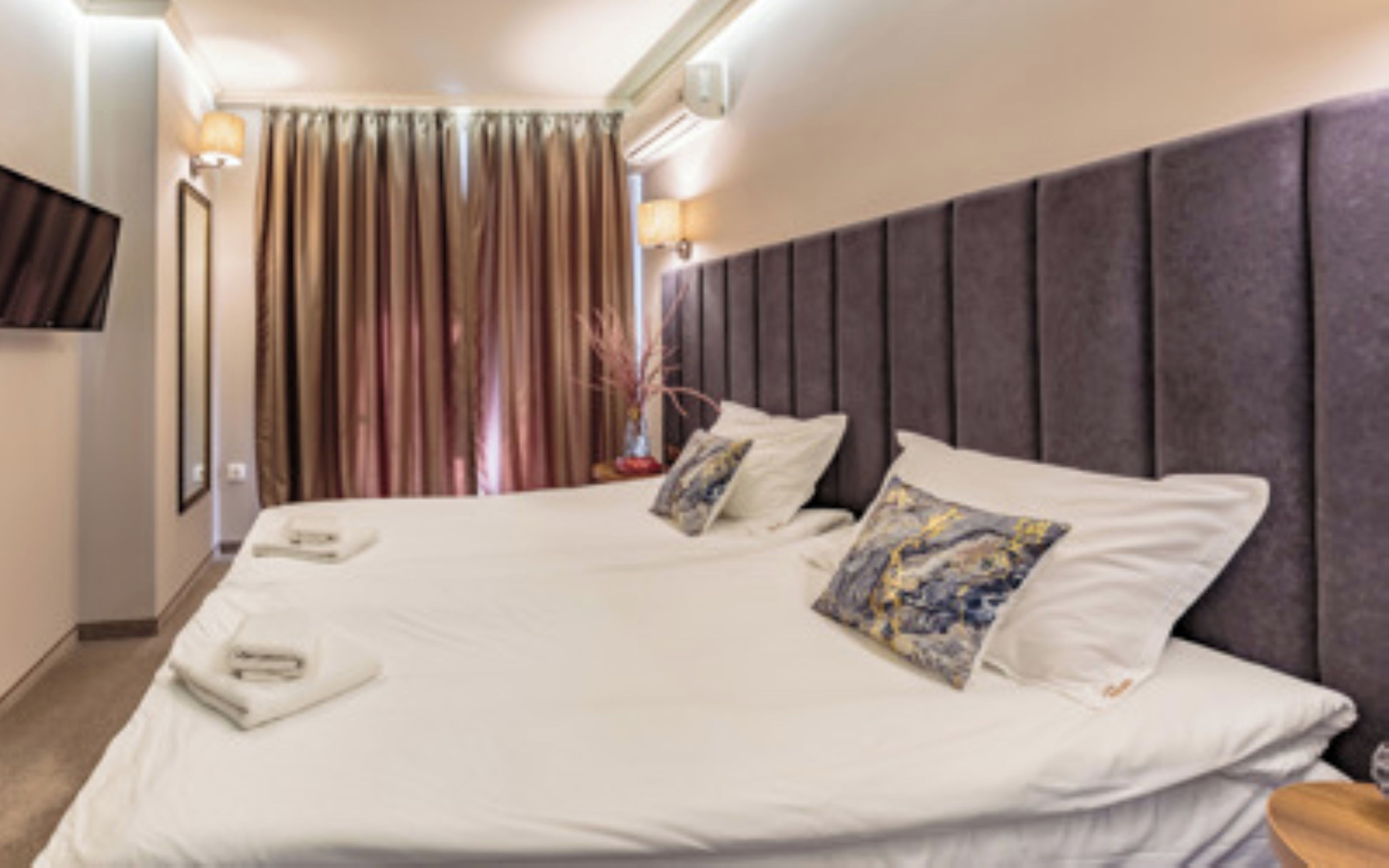 Une chambre d’hôtel avec un grand lit, un téléviseur à écran plat fixé au mur et une fenêtre avec des rideaux.