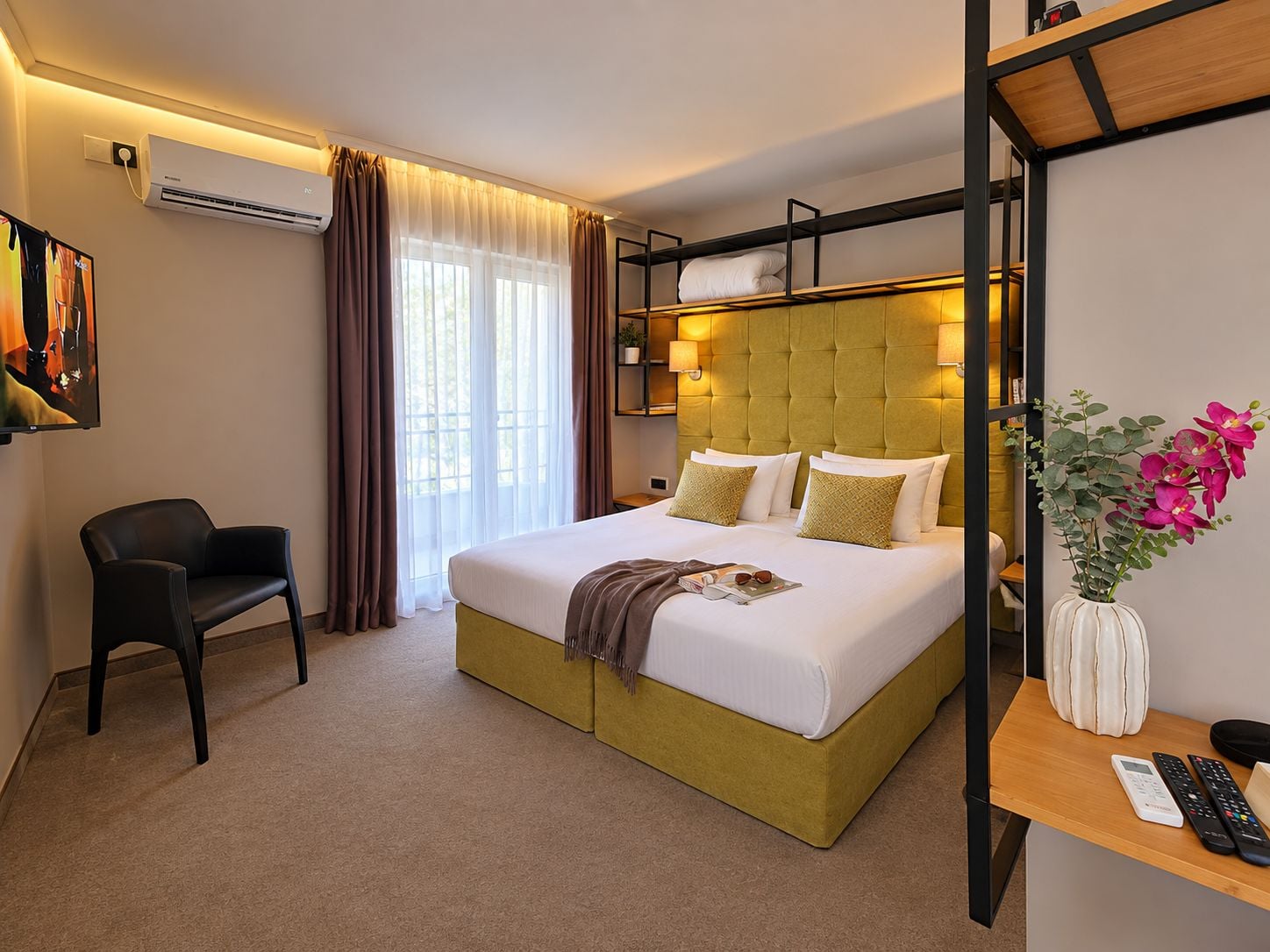 Une chambre d’hôtel avec un lit, une chaise, un bureau agrémenté d’un vase de fleurs et un téléviseur.