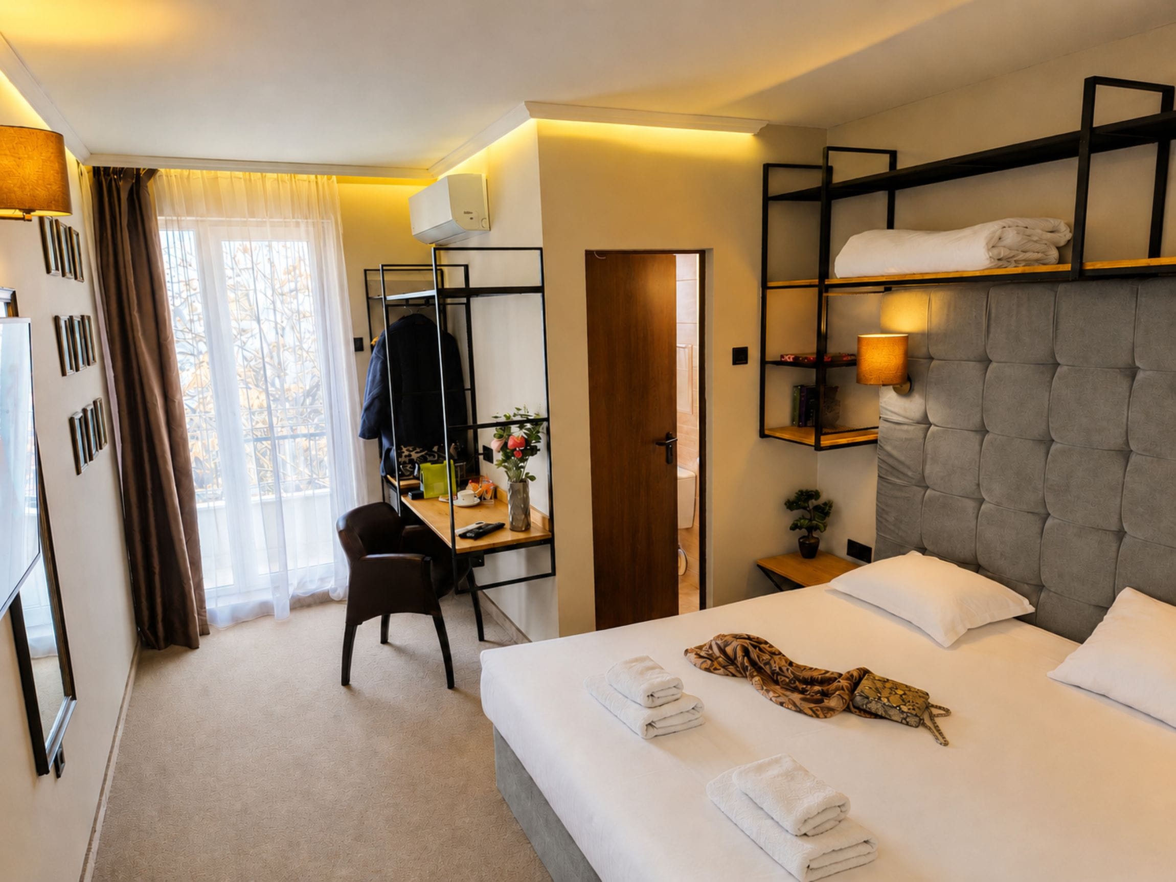 Habitación de hotel con cama, escritorio, silla, armario y ventana con cortinas.