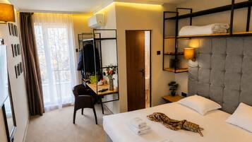 Habitación de hotel con cama, escritorio, silla, armario y ventana con cortinas.