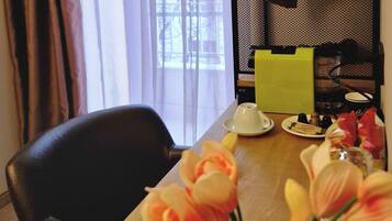 Habitación de hotel con una mesa de madera, un control remoto, un florero con flores y una ventana con cortinas.