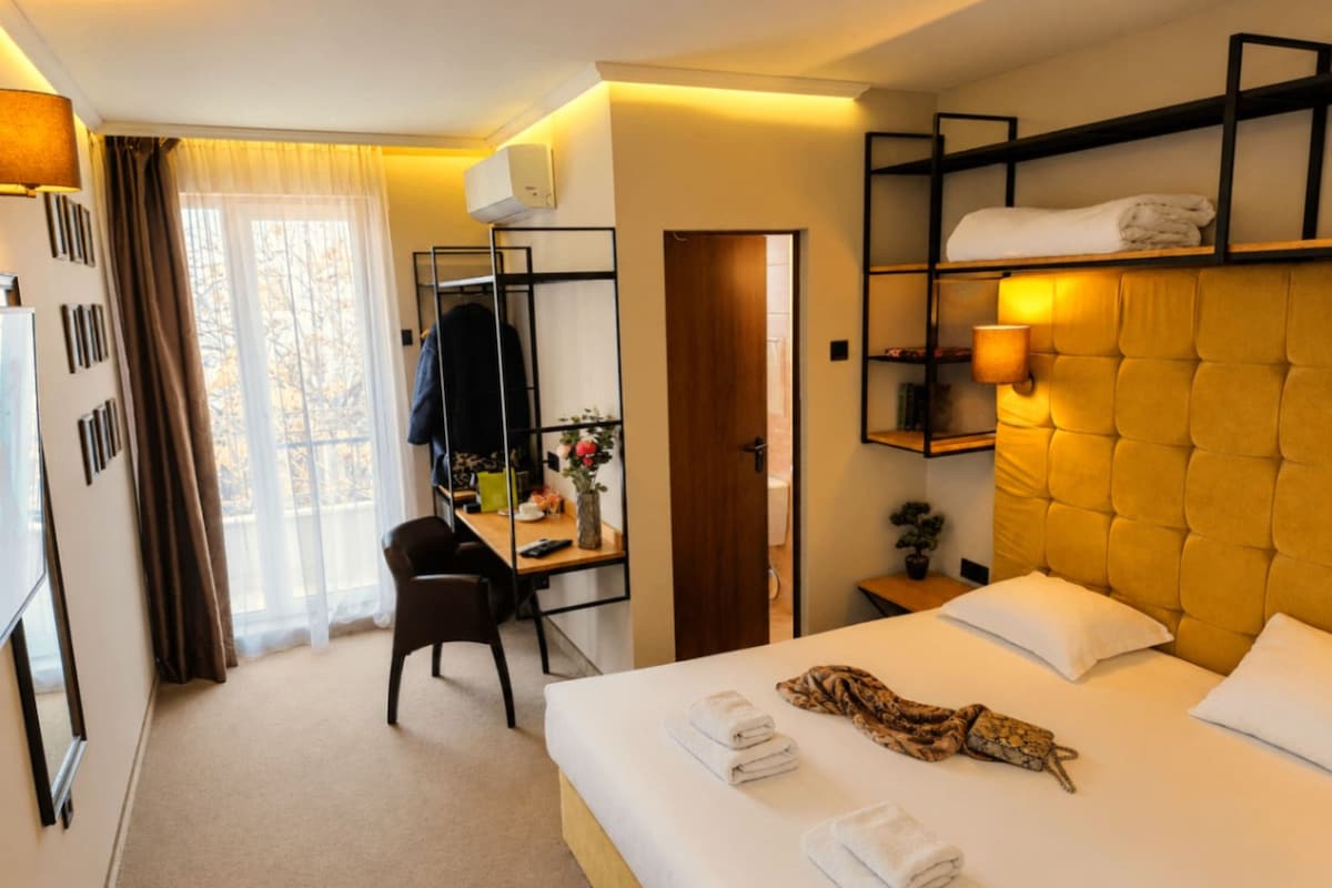 Quarto de hotel com cama, escrivaninha, cadeira, guarda-roupa e porta do banheiro.