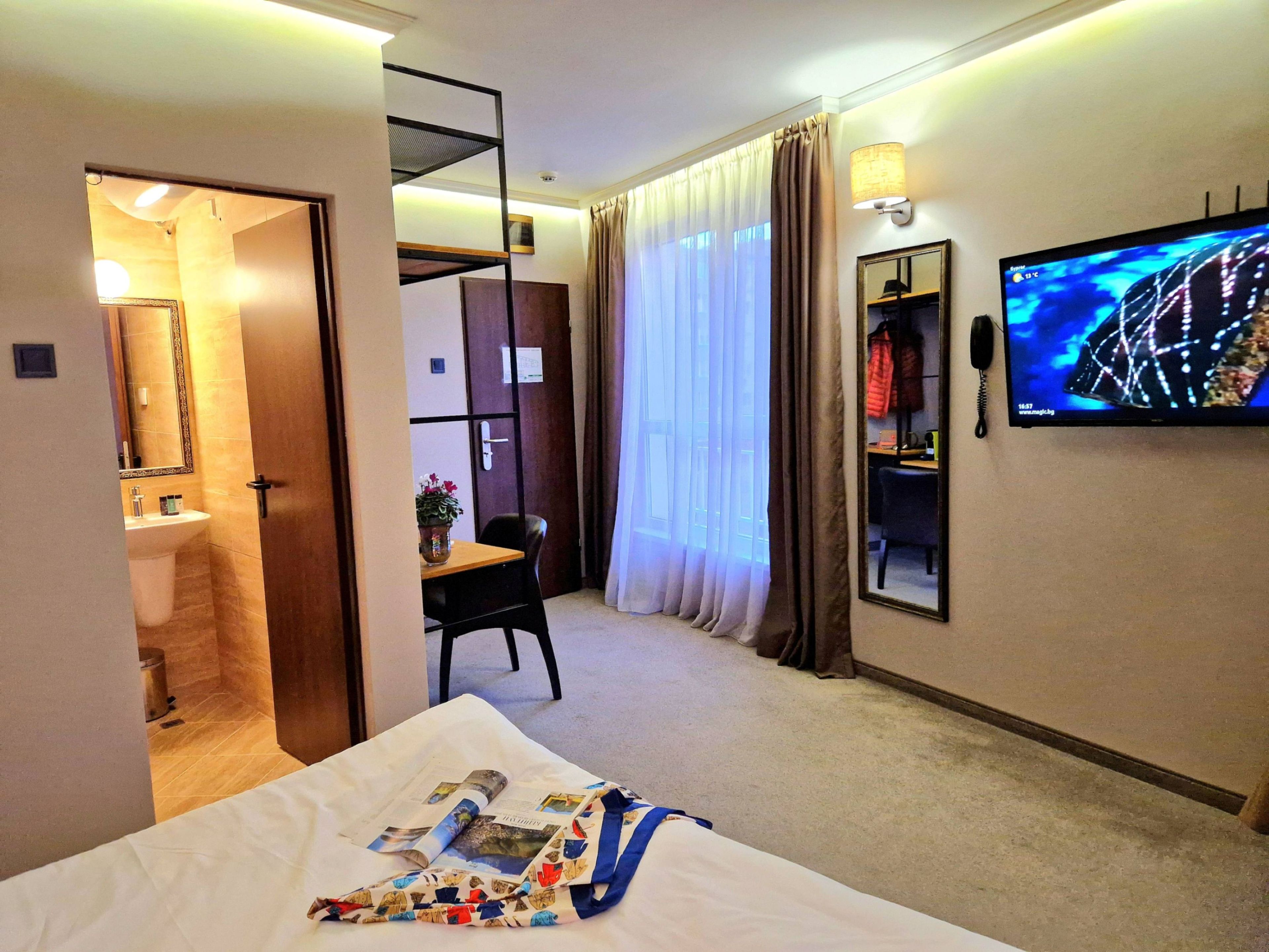 A hotel room with a bed, a desk, a chair, a television, and a bathroom visible through an open door.
