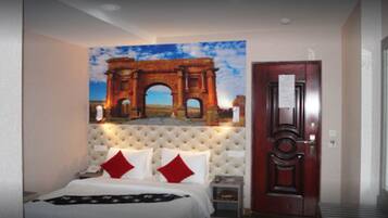 Een hotelkamer met een groot bed, een gestapeld hoofdeinde en een schilderij van een oude boog.