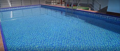 Una piscina con borde de azulejos y escalera de metal.