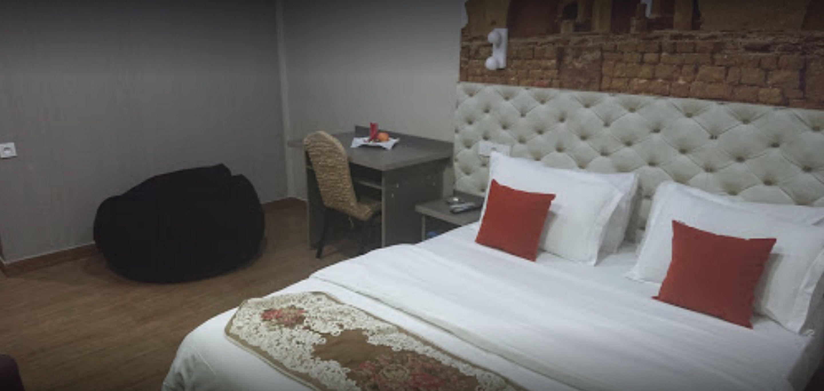 Quarto com cama, cadeira, mesa e parede de tijolos.