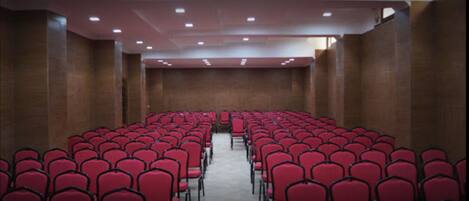 A conference room with rows of red chairs and a high ceiling with recessed lighting.