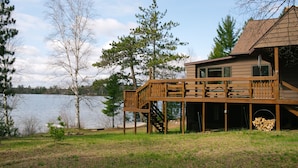 A cabin with a wooden deck overlooking a lake, surrounded by trees. - Little Lake Cottage in Gwinn: Sun, Swims & S'mores – Your Summer Starts Here (Gwinn)