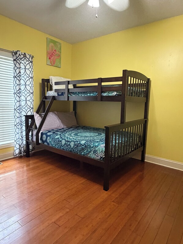 Una cama litera en una habitación con piso de madera, paredes amarillas y ventilador de techo.