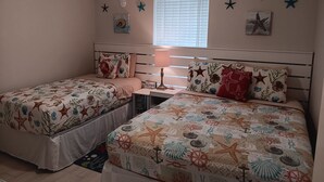 Une chambre avec deux lits, une table de chevet, une lampe et des étoiles de mer décoratives accrochées aux murs.