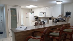 Une cuisine moderne avec des meubles blancs, un îlot central doté de tabourets, un réfrigérateur, un four à micro-ondes et une cuisinière.