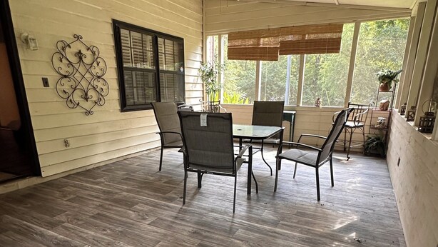 Ein überdachter Patio-Bereich mit Esstisch und Stühlen, einem Deckenventilator und Blick auf die grüne Umgebung.