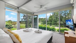 Camera da letto moderna con un letto grande, una TV a schermo piatto e vista su un giardino rigoglioso.