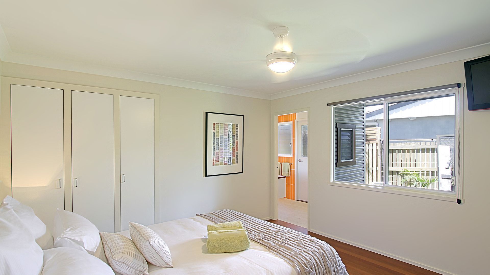 A bedroom with a bed, pillows, a framed picture, a ceiling fan, and a window with blinds.