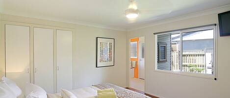 A bedroom with a bed, pillows, a framed picture, a ceiling fan, and a window with blinds.