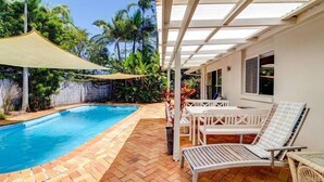 A swimming pool with a herringbone tile pattern, surrounded by a wooden deck and a covered patio area with white furniture. - 'No-Steps Noosa' - Home Away From Home 🏠  (Noosa Heads)