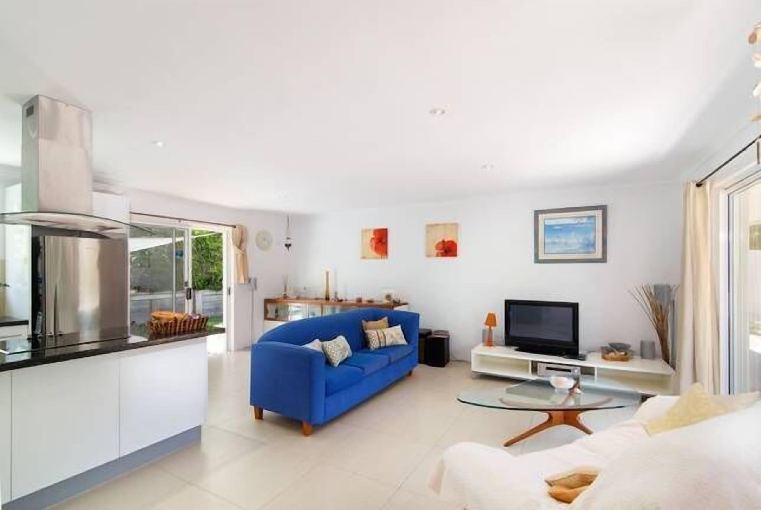 A modern living room with a blue sofa, a flat-screen TV, and a glass coffee table.