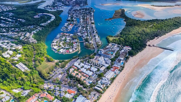 An aerial view of a coastal resort with a beachfront, a marina, and a dense cluster of buildings. - 'No-Steps Noosa' - Home Away From Home   🏠  (Noosa Heads)
