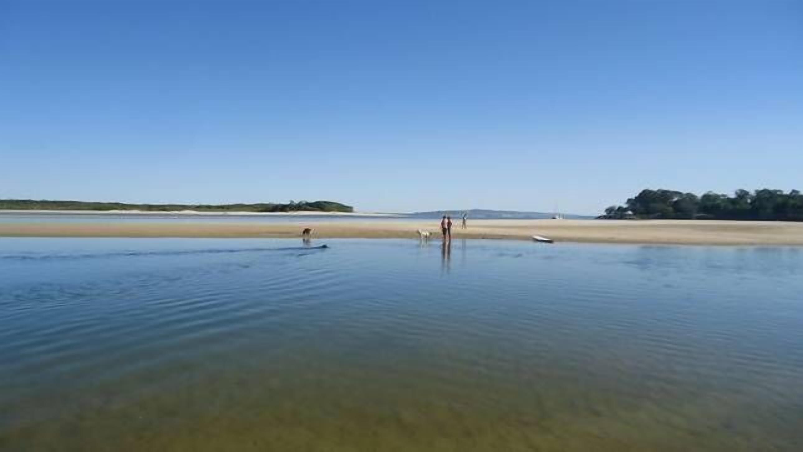 Een strand met helder water, een zandstrand en enkele mensen.