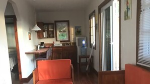 Un salon avec un plancher en bois, un canapé et une table basse. Il y a également un coin cuisine avec des placards et un réfrigérateur.
