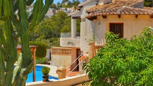 Una villa de estilo mediterráneo con piscina, terraza de madera y vistas a las colinas circundantes.