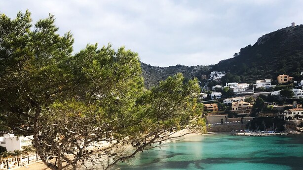 Vista costera con aguas turquesas cristalinas, una playa y una ladera con edificios.