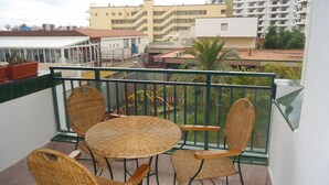 Un balcon doté de meubles en osier, d’une rambarde en verre et offrant une vue sur les bâtiments en arrière-plan.