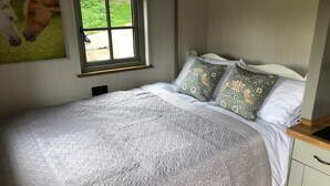 Ein Schlafzimmer mit einem großen Bett, Kissen mit floralem Muster, einem Fenster mit Blick auf Grünflächen und einem Wandbild von Pferden.