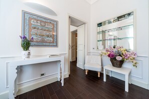 Un pasillo con una consola blanca, una obra de arte enmarcada, un banco blanco y un cesto de flores.