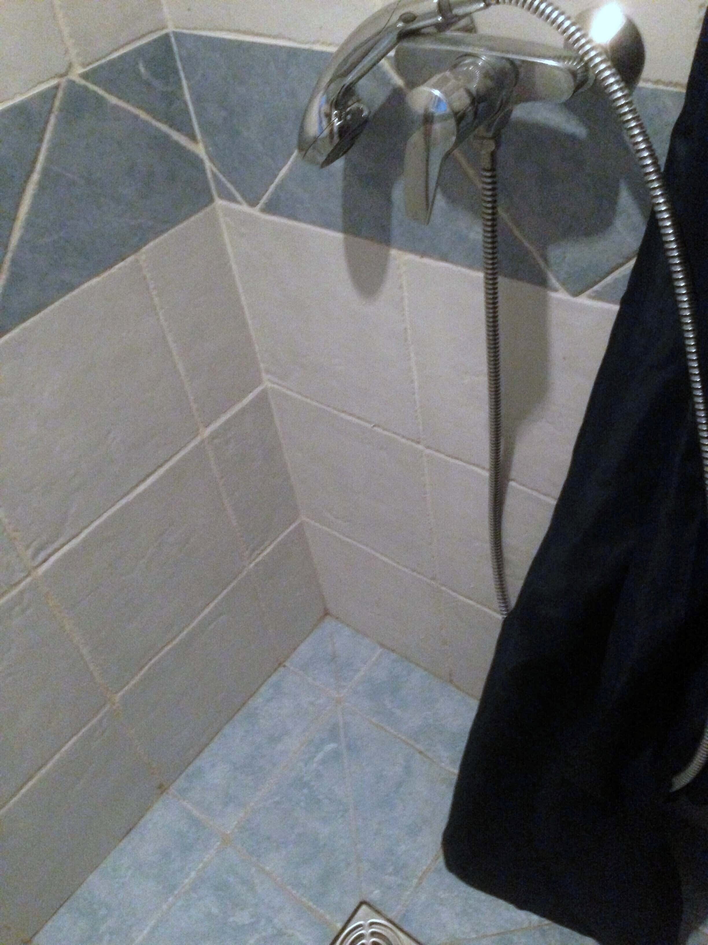 Een badkamer met douchegedeelte, betegelde wanden en een afvoer.
