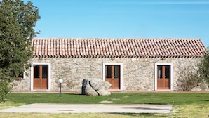 Un bâtiment en pierre avec un toit en tuiles, deux portes en bois et un grand rocher au premier plan.
