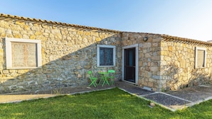 Un bâtiment en pierre avec un toit en tuiles, une petite pelouse et deux fenêtres ornées de grilles décoratives.