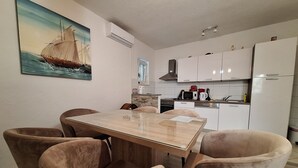 A modern kitchen with white cabinets, a microwave, and a coffee maker. There is a dining table with chairs and a painting of a sailboat on the wall. - App with jacuzzi, fitness near old town (Trogir)