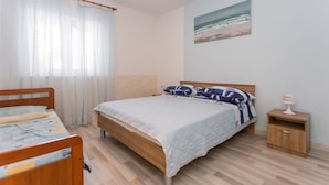 A bedroom with a bed, a bedside table, a nightstand, a window with sheer curtains, and a painting of a beach scene. - App with jacuzzi, fitness near old town (Trogir)