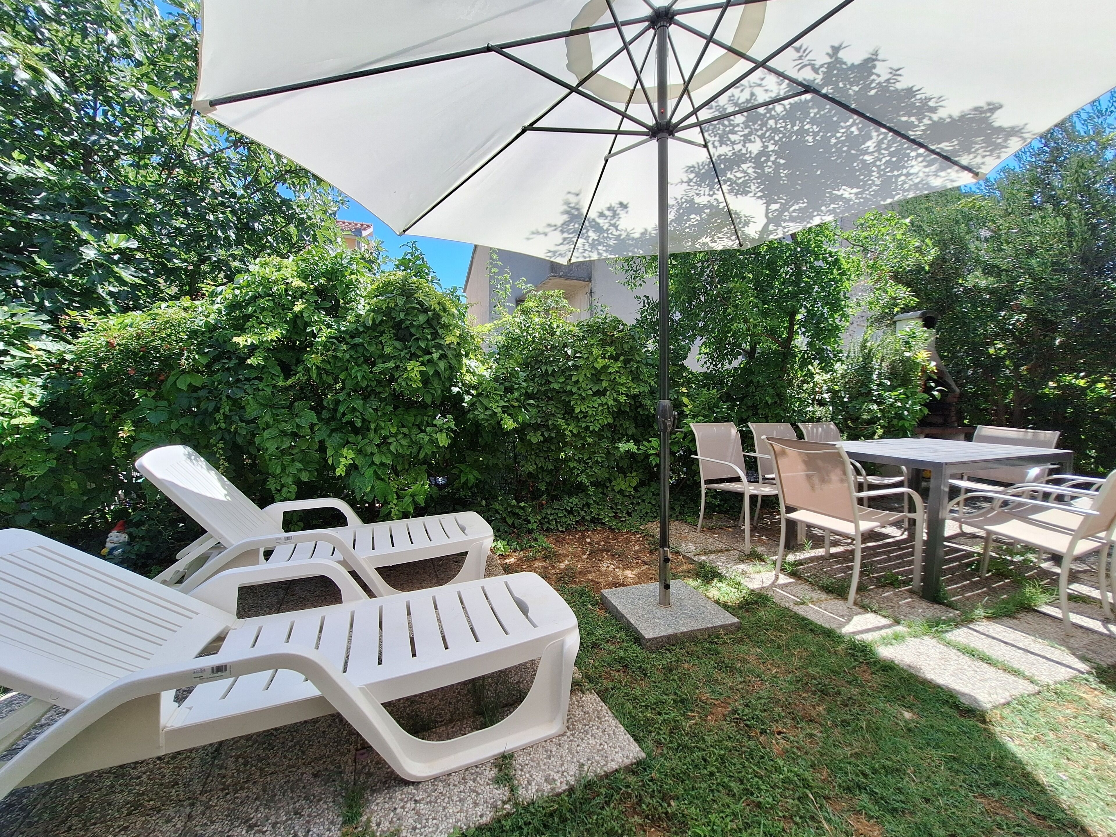 Eine Terrassenfläche mit Liegestühlen, einem Tisch und einem Sonnenschirm.