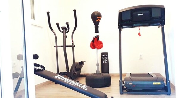 Un gimnasio en casa con cinta de correr, bicicleta estática, elíptica, saco de boxeo y banco de pesas.