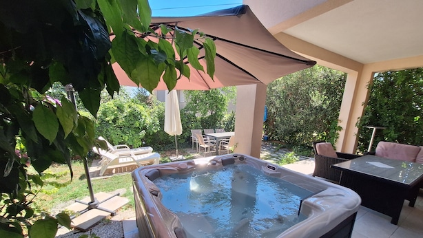 A hot tub in a covered outdoor area with patio furniture and greenery. - App with jacuzzi, fitness near old town (Trogir)