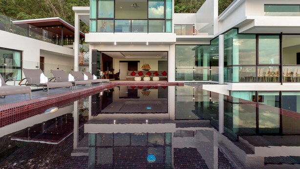 Een modern huis met een zwembad, buitenmeubels en grote ramen.