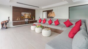 Een moderne woonkamer met een grijze bank, rode kussens en een houten accentmuur. Er staan drie ronde salontafels met decoratieve objecten.