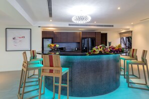 A modern kitchen with a central island, bar stools, and a decorative fruit arrangement.