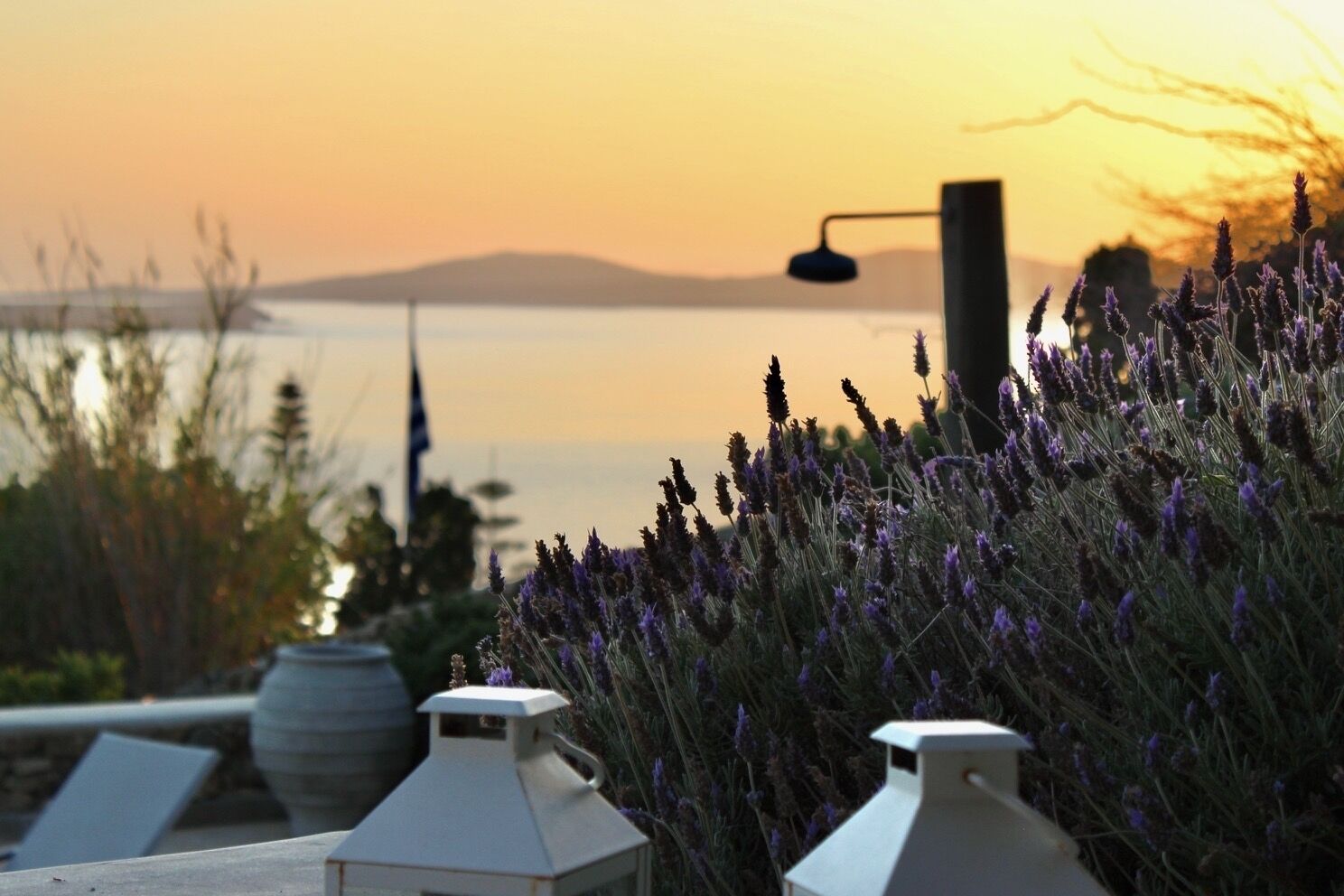 A sunset view with a body of water, mountains in the distance, and a row of white lanterns in the foreground.