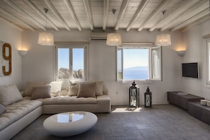 Sala de estar moderna com um sofá seccional bege, uma mesa de centro redonda e uma janela grande com vista para o mar.
