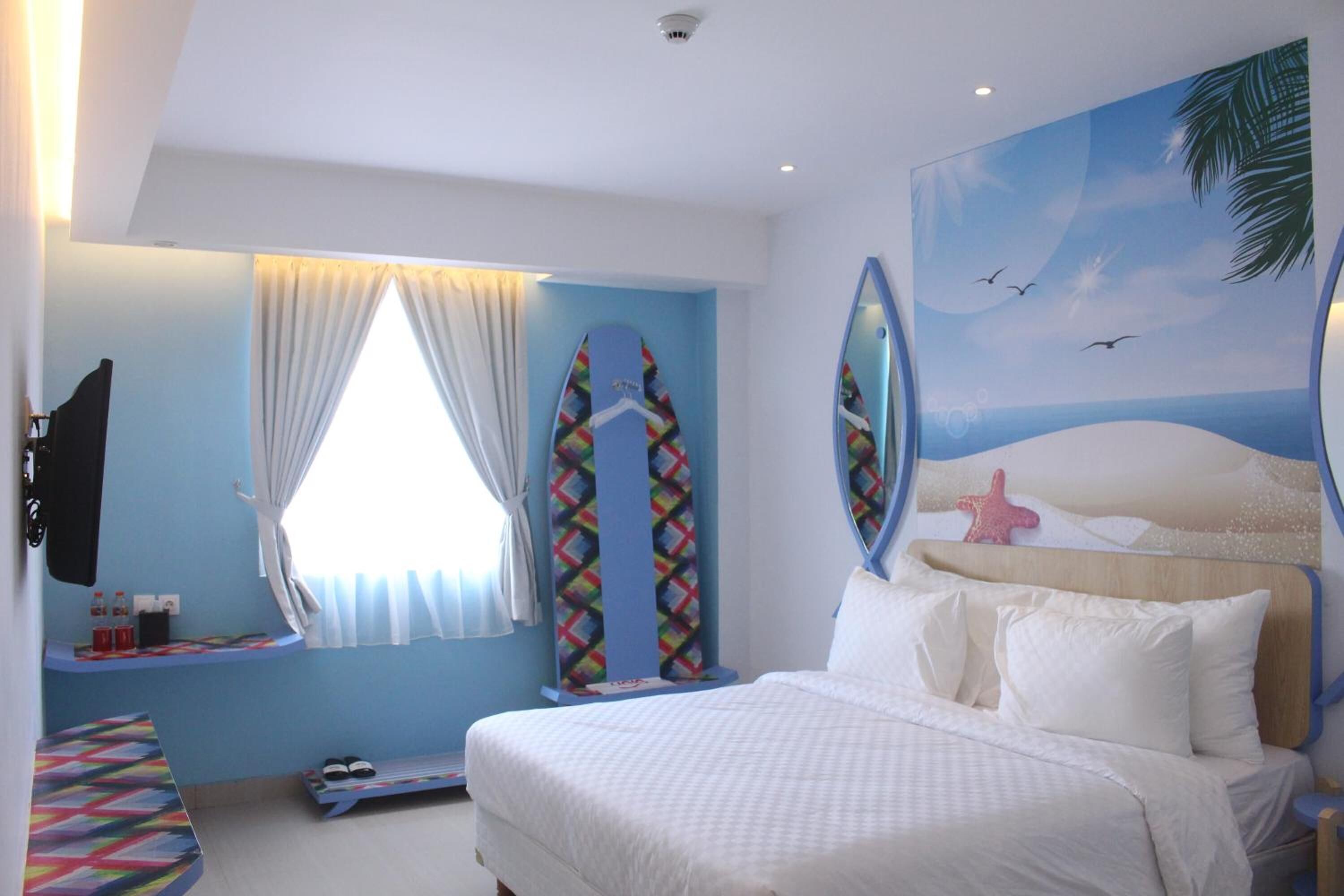 A hotel room with a bed, a window with curtains, a wall-mounted TV, and a beach-themed mural.