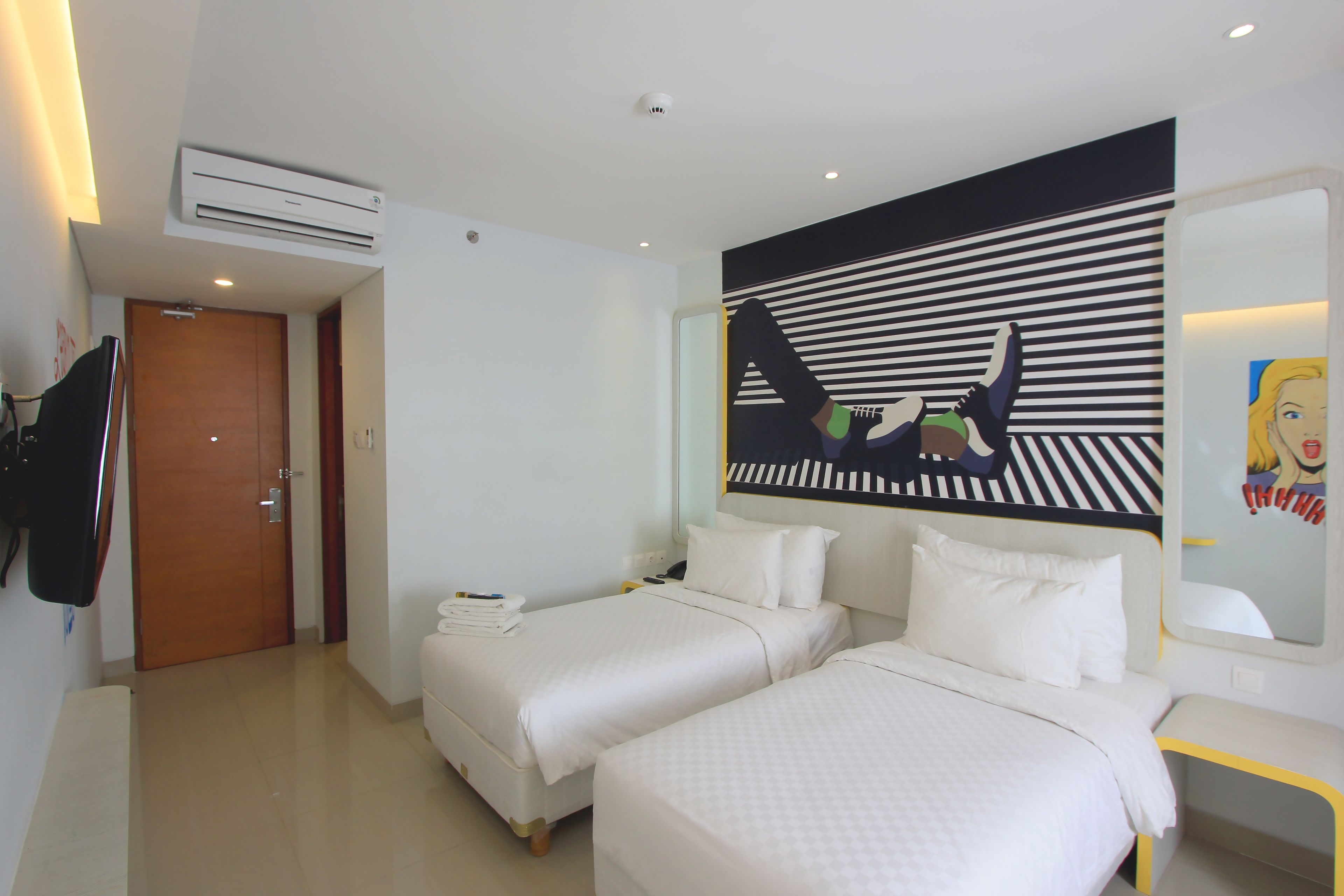 Habitación de hotel con dos camas, un televisor de pantalla plana, un equipo de aire acondicionado y un espejo grande con diseño de pared a rayas.