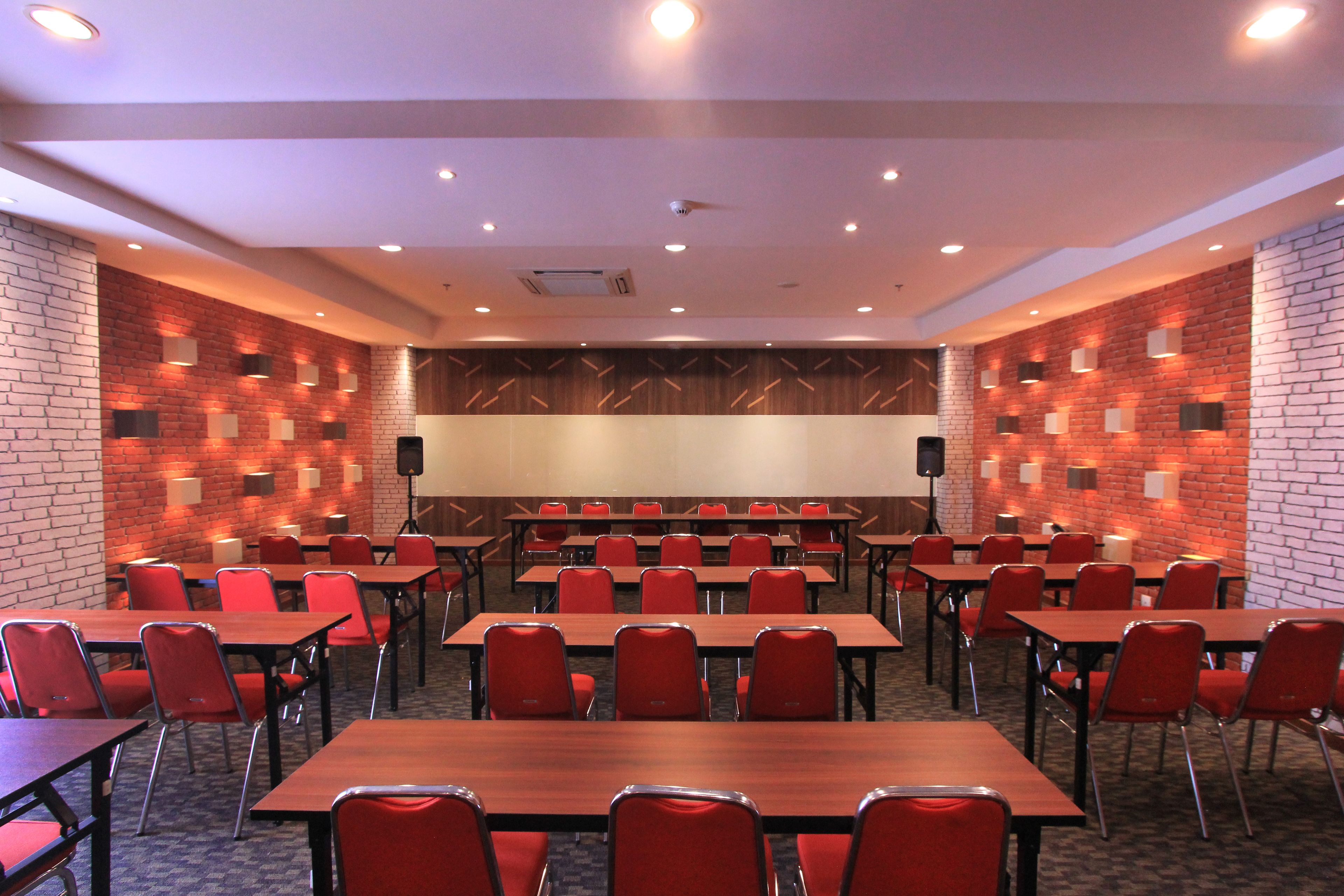 A conference room with tables and chairs, a projector screen, and a brick wall with patterned lighting.