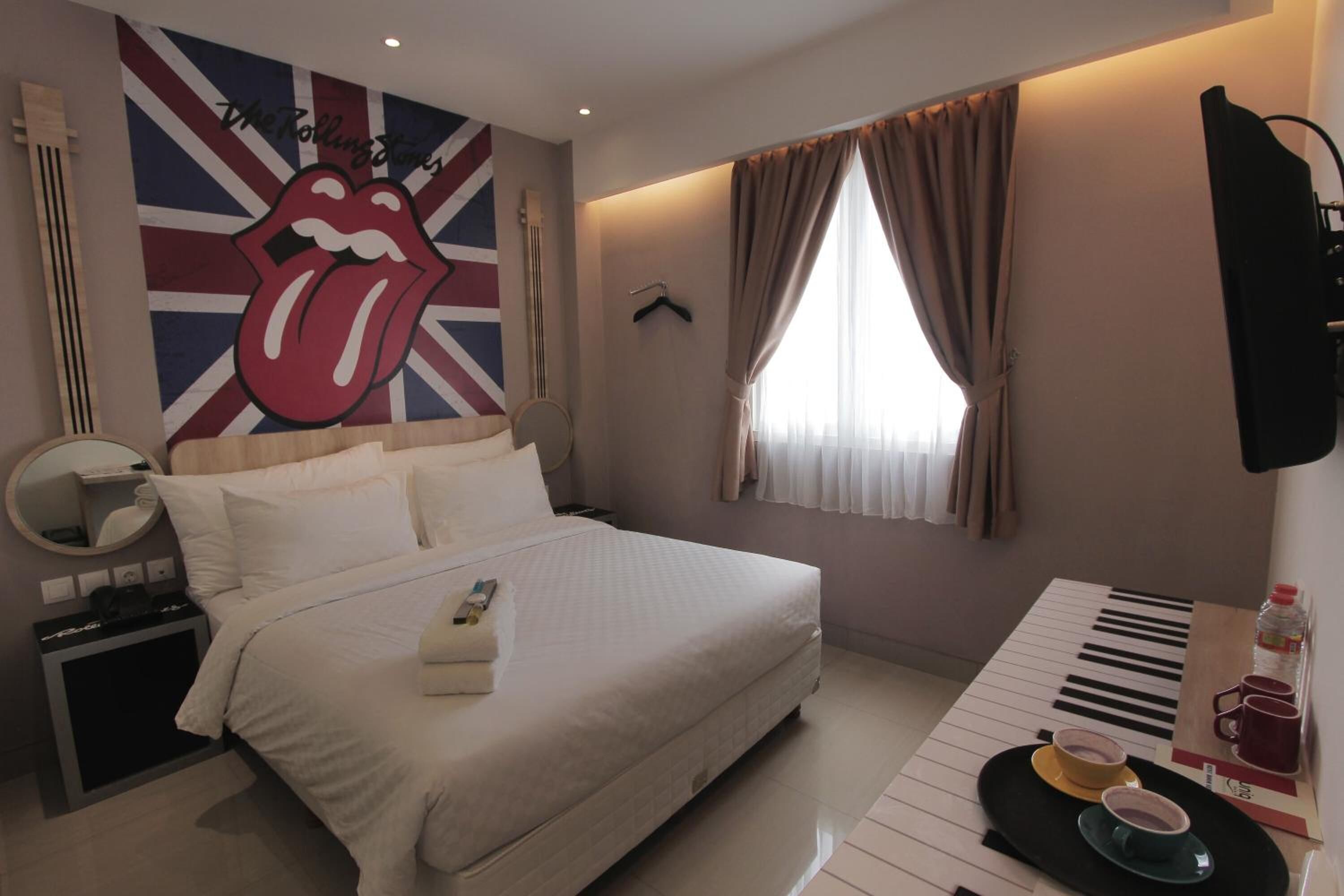 A bedroom with a bed, a piano, a mirror, a towel, and a Rolling Stones mural.