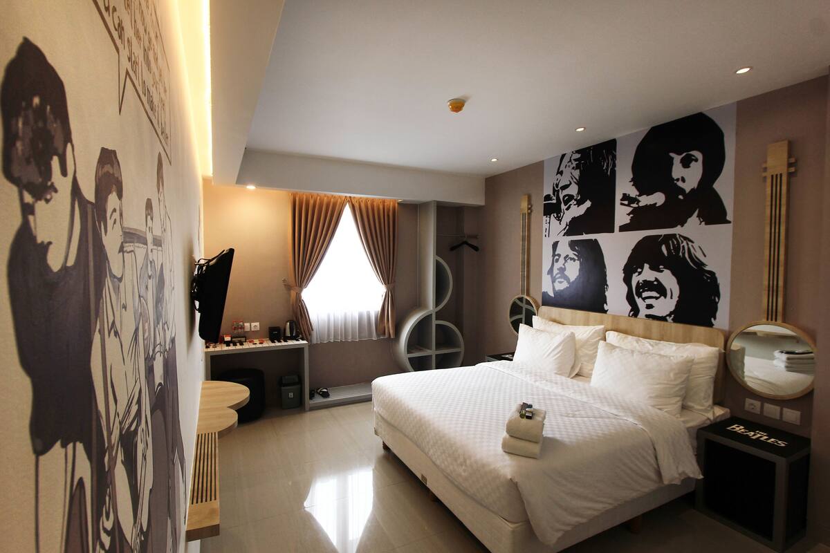 Una habitación de hotel moderna con una cama grande, una mesita de noche, un espejo y obras de arte en las paredes.
