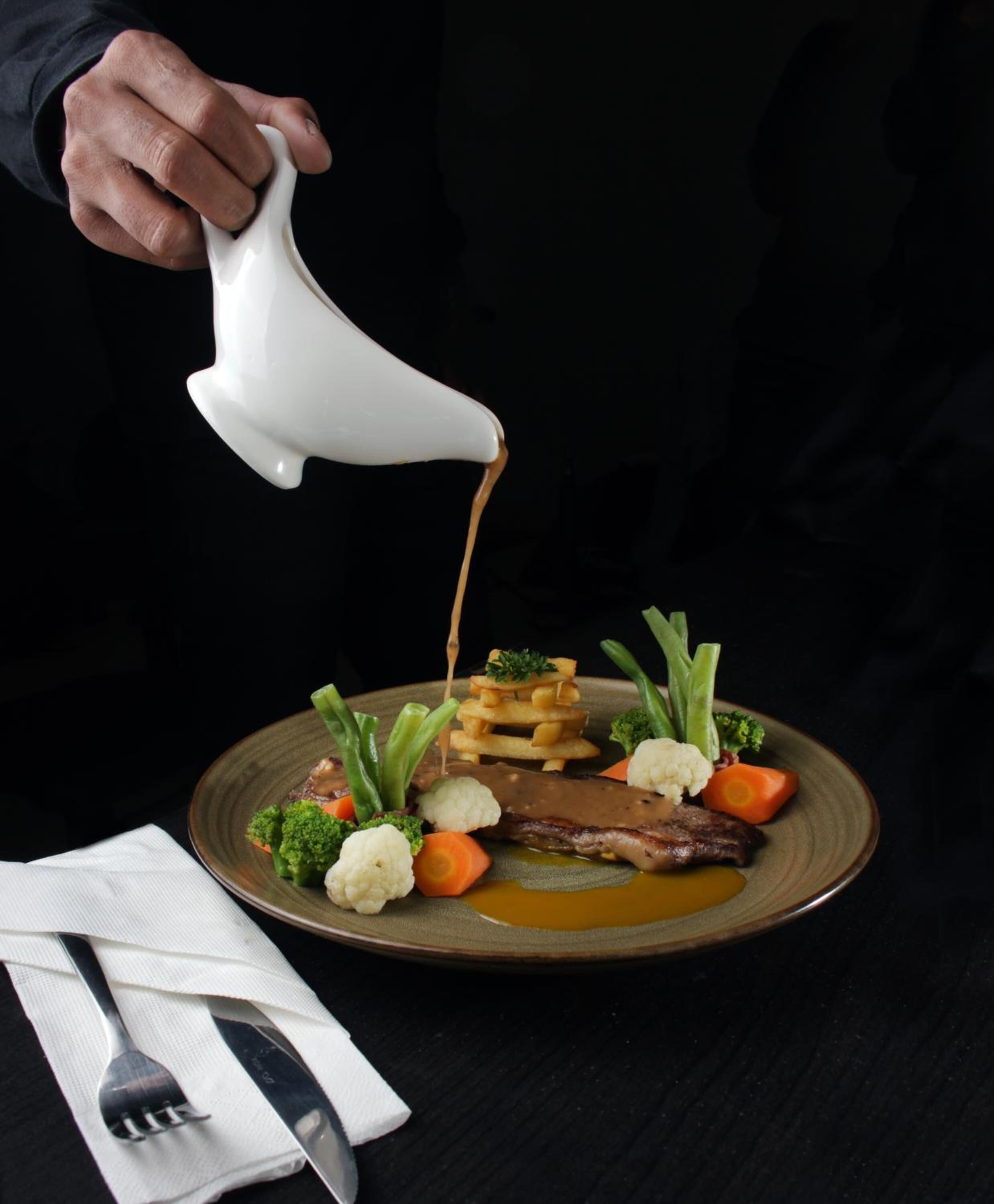 Una persona sirviendo salsa sobre un plato de comida.
