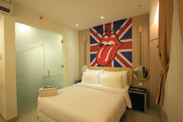 Quarto de hotel com uma cama, divisória de chuveiro de vidro, parede com o logotipo dos Rolling Stones, mesa de cabeceira e um espelho.