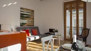 A modern living room with a sofa, a dining table with chairs, a TV, and a painting on the wall. - Singular Stays El Balcon de Manet (Valencia / València)